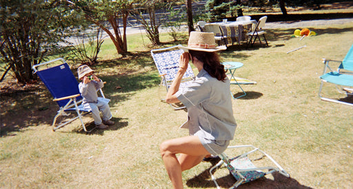 A woman and child taking photos of each other sitting on chairs in a park.