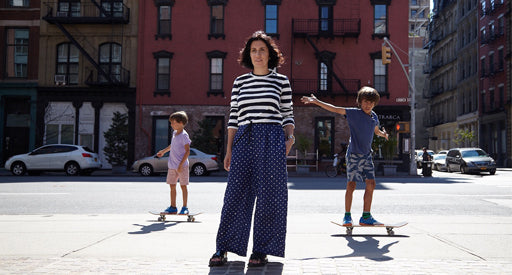 Woman standing in front of an apartment building surrounded by two boys skateboarding.