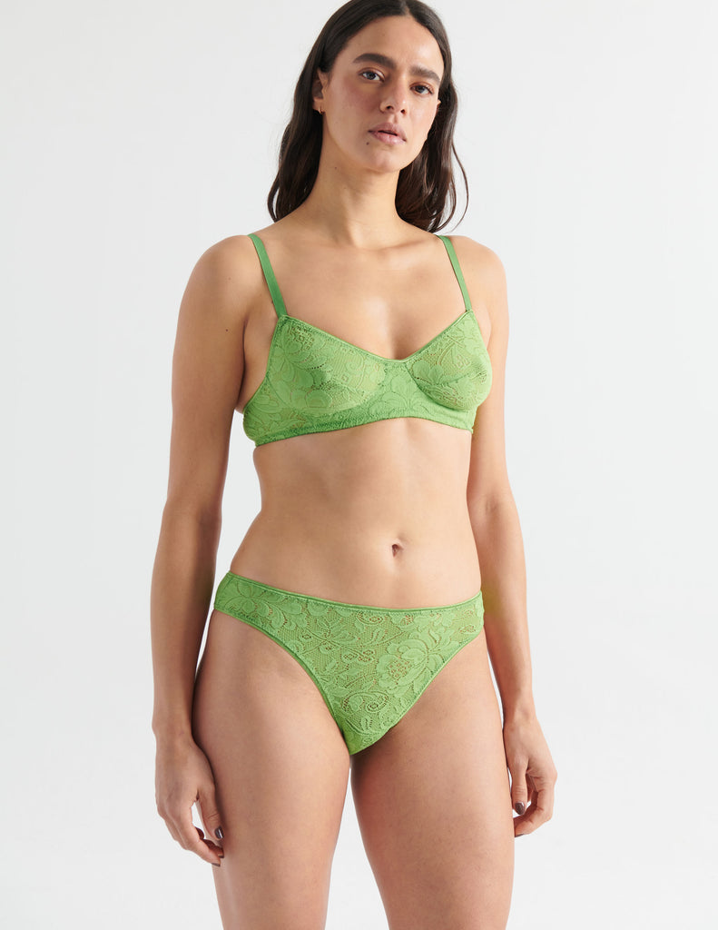 Three quarter view image of model wearing green lace thong with matching bralette. 