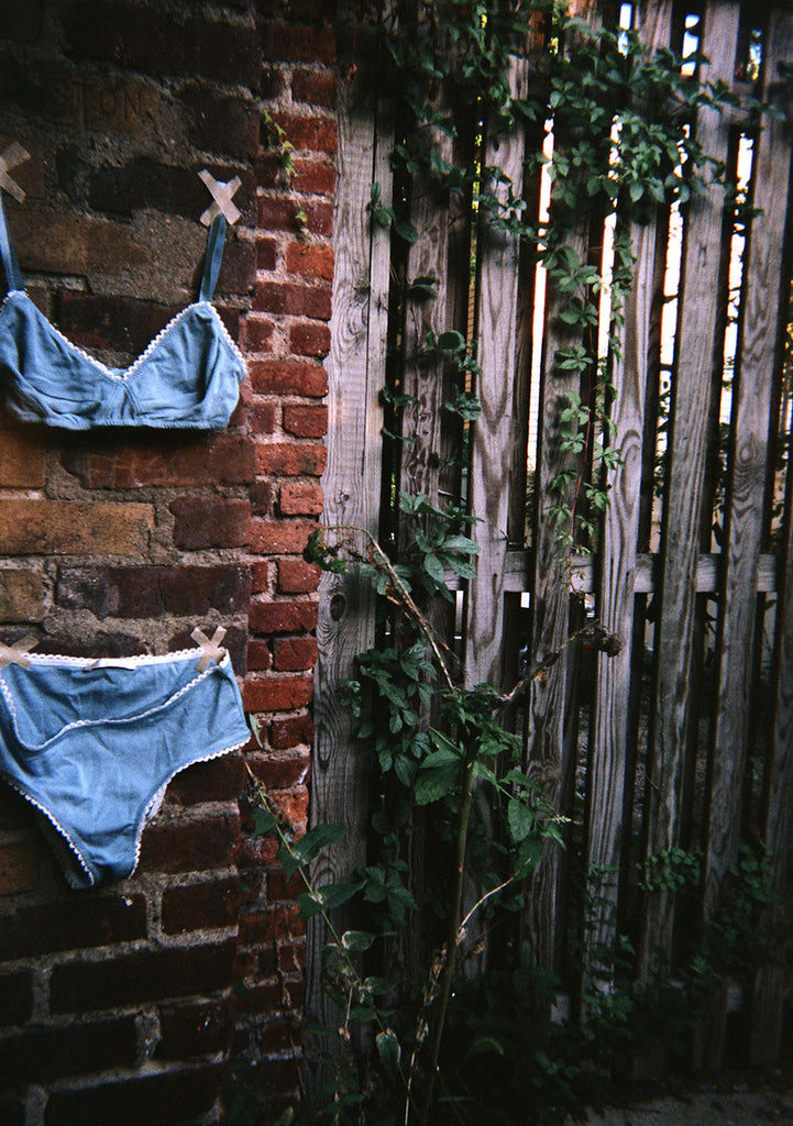 Blue bralette with white trim and matching panty taped to a brick wall. 