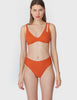 Front view of woman wearing an orange bikini top with asymmetric crisscross straps with matching bottoms