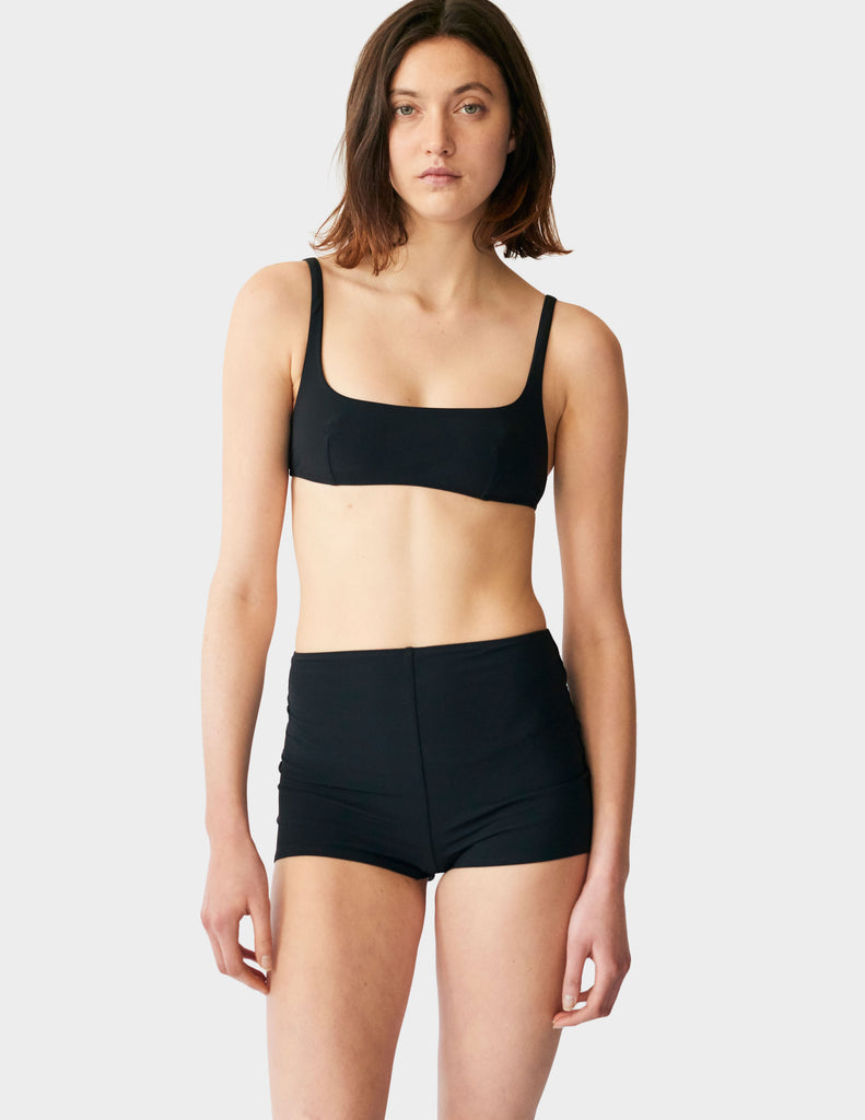 Woman wearing a black mid-rise swim short bottoms with matching bikini top