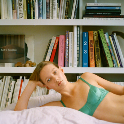 A model laying in front of a book shelf wearing a green Gita bra.