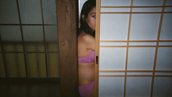 Woman in a pink bra and underwear viewed through a door crack.