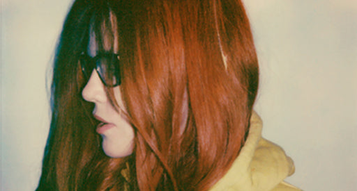 Up close side view of a red haired woman with glasses against a blank wall.