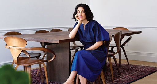 Araks in a blue dress sitting at a wooden dining table.