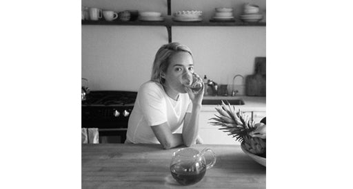 Black and white photo of a woman drinking from a glass in a kitchen.