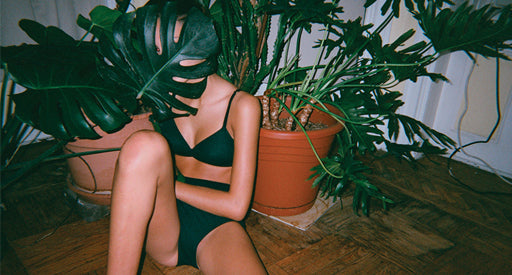 Woman in black underwear and bra surrounded by green plants.
