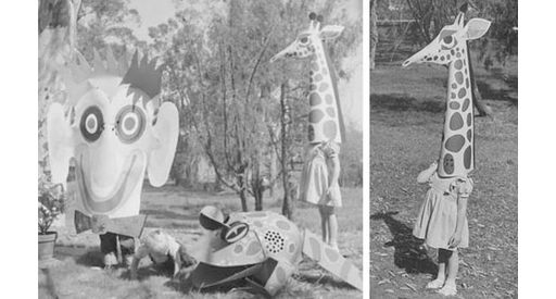 Black and white photo of a large paper monkey, frog and giraffe heads on kids.