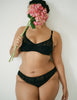 woman wearing black waverly bra holding flowers by a white wall 