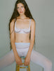 A model wearing the araks silk gita underwire bra and gwyneth panty in fairy lavender sitting on a stool.