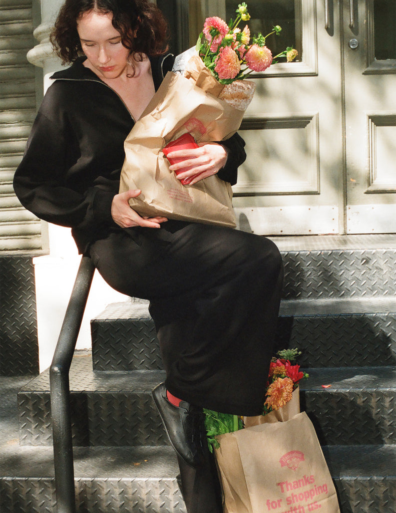 A model wearing the Araks black Vivienne half zip sweatshirt and matching black Vero sweatpants