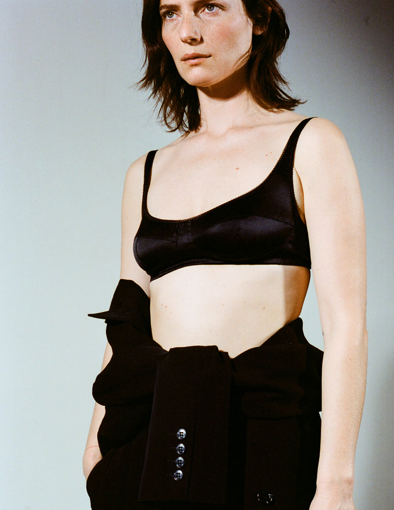 woman wearing a black penelope bra with a black blazer tied around her waist. 