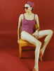 Woman in a purple Araks swimsuit sitting on a chair against a red background