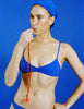 Woman in a blue Araks Tessa bikini and blue swim cap against a blue background
