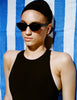Person wearing sunglasses and a black outfit on a blue and white striped towel