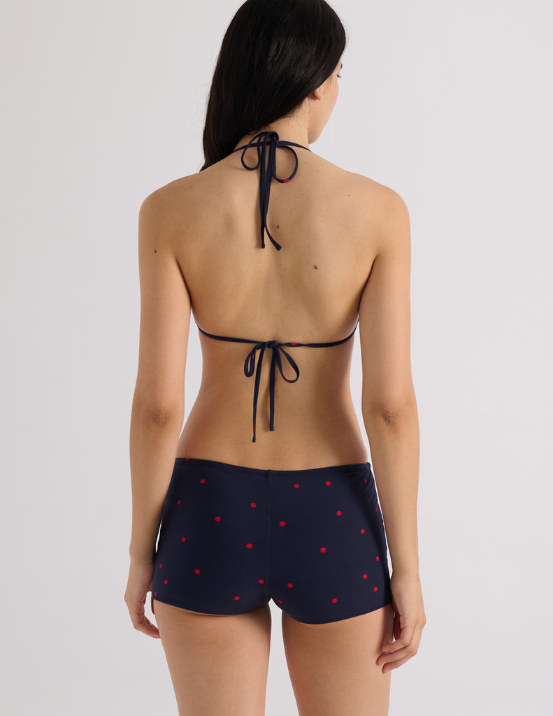 Model wearing Araks Nelle bikini top and Polly swim shorts in navy with red polka dots