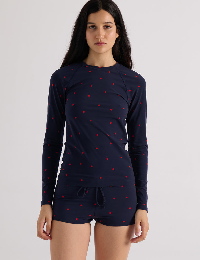 Model wearing Araks Undine rashguard with Polly swim shorts in navy with red polka dots