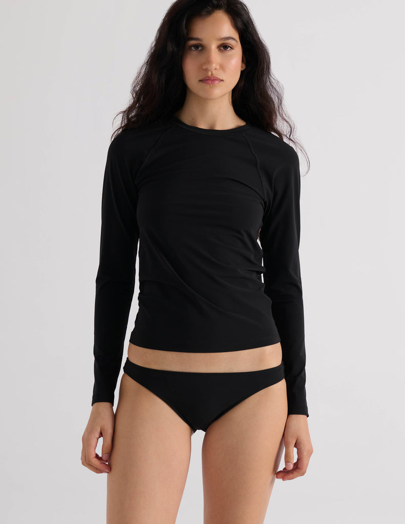 Model wearing the Araks Undine Rashguard in Black, a long-sleeve fitted rash guard with a crew neck, paired with black bikini bottoms, against a white background