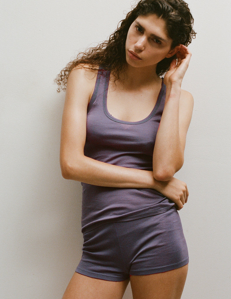 A model wearing a James tank top and Presley shorts in Violette, standing against a plain light gray wall.