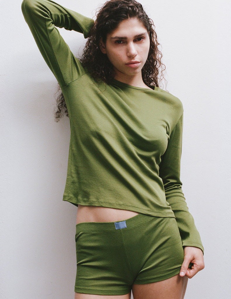 A model wearing the Sabine long sleeve top and the Presley short in Moss posed against a plain light gray wall.