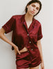 A woman modeling the Araks Shelby silk pajama top with the Tia pajama shorts in Garnet against a light gray studio background