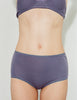 A model wearing Araks Mabel hipster and Antonia bralette in Violette posed against a plain light gray background.