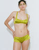 A model wearing the Araks Penelope bralette in the shade chartreuse, posing against a white wall. 