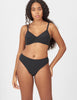 A woman modeling a two-piece black bikini set against a plain light gray studio background.