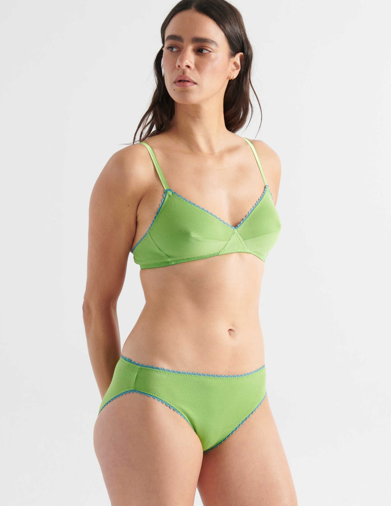 Three quarter view image of model wearing green bralette with blue trim with matching panties. 