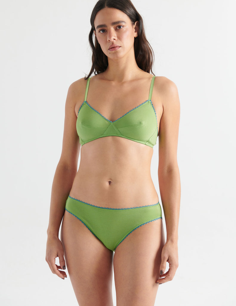 Front view image of model wearing green bralette with blue trim with matching panties. 