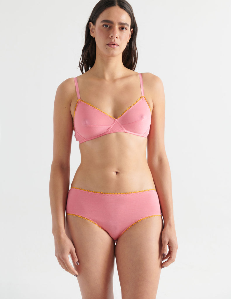 Front view image of model wearing pink bralette with yellow trim and matching hipster panties. 