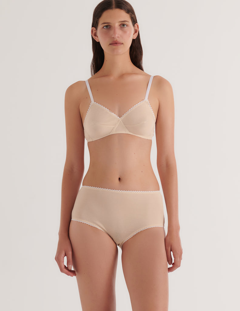 Woman wearing a beige Antonia bralette and mabel hipster set on a white background