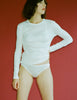 Person wearing an Araks 100% Organic Cotton white long-sleeve tee with white panties against a red background