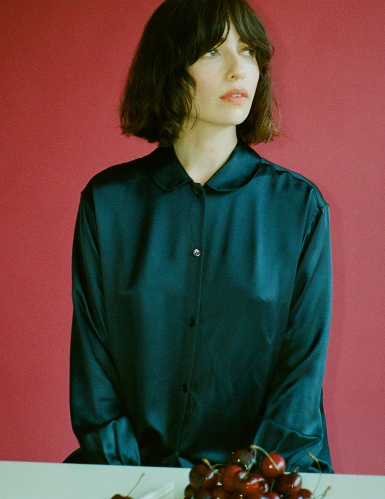 Person wearing a dark blue silk shirt against a red background