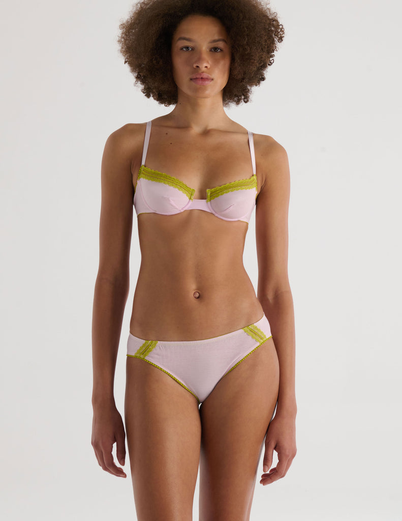 A model in the araks chloe underwire bra and sonja panty in confection pink with chartreuse lace trim