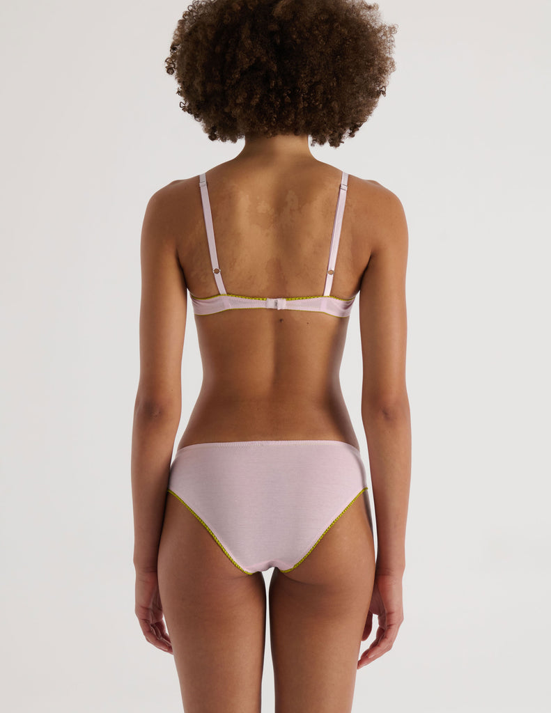 A model in the araks chloe underwire bra and sonja panty in confection pink with chartreuse lace trim