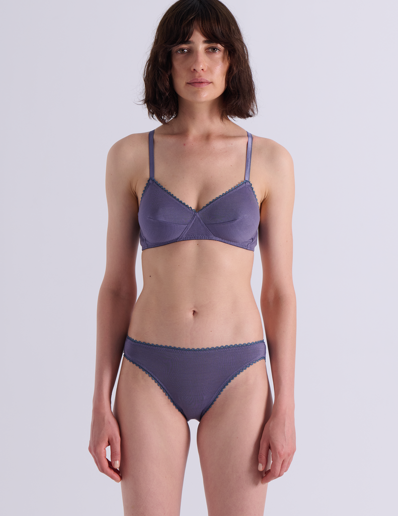 A model wearing Araks Antonia bralette and isabella panty in Violette against a light gray studio background.