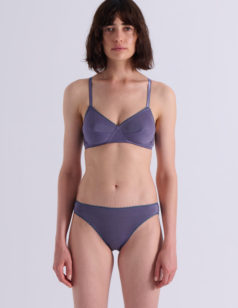 A model wearing Araks Antonia bralette and isabella panty in Violette against a light gray studio background.