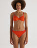 Person wearing an Araks orange organic cotton Antonia Bralette and Stella thong set on a white background
