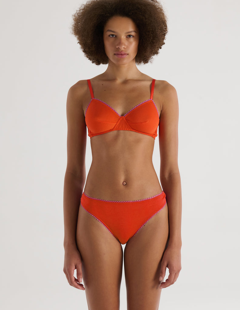 Person wearing an Araks orange organic cotton Antonia Bralette and Stella thong set on a white background