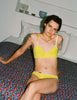 woman wearing a yellow araks organic cotton antonia bralette  while sitting on bed. 