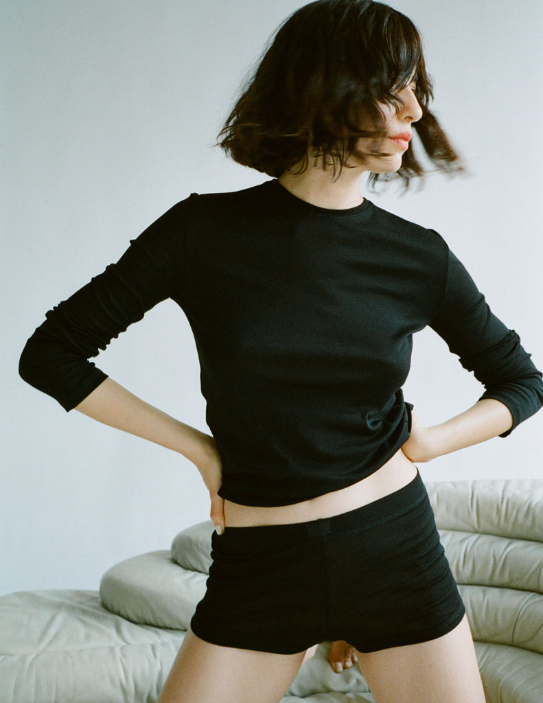 A model on the couch in the araks 100% organic cotton sabine long sleeve t shirt and presley short in black
