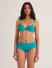 woman wearing araks organic cotton sofia bra in color parrot blue against white wall