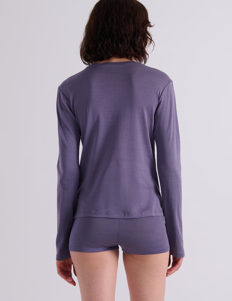 A model wearing a Sabine long sleeve top and Presley shorts in Violette, standing against a plain light gray wall.