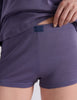 A model wearing a Sabine long sleeve top and Presley shorts in Violette, standing against a plain light gray wall.