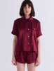 A woman modeling the Araks Shelby silk pajama top with the Tia pajama shorts in Garnet against a light gray studio background