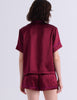 A woman modeling the Araks Shelby silk pajama top with the Tia pajama shorts in Garnet against a light gray studio background