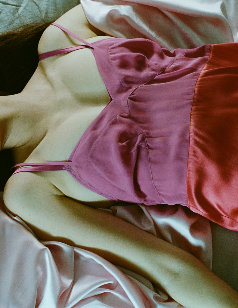 A model lying in a bed wearing the Araks two toned pink silk Holly slip.