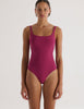 Woman wearing a purple Araks swimsuit against a white background